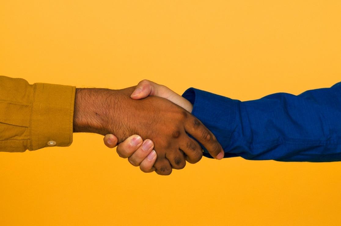 Two people shaking hands, one wearing a yellow shirt and the other a blue shirt, with a solid yellow background.